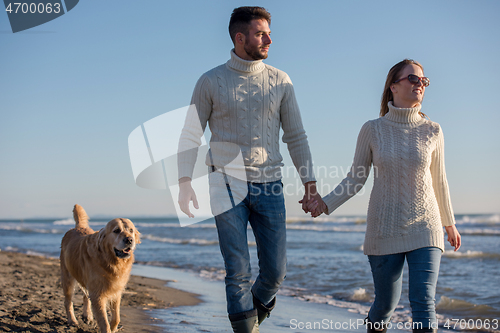 Image of couple with dog having fun on beach on autmun day