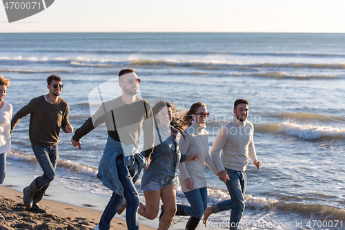 Image of Group of friends running on beach during autumn day