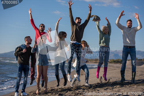 Image of young friends jumping together at autumn beach