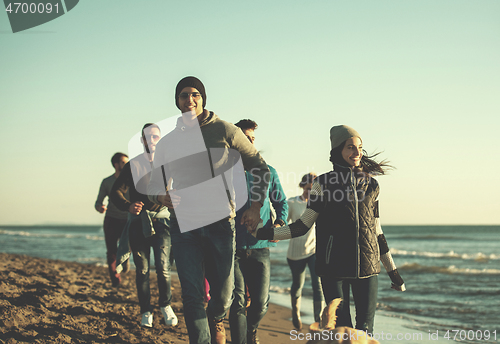 Image of Group of friends running on beach during autumn day