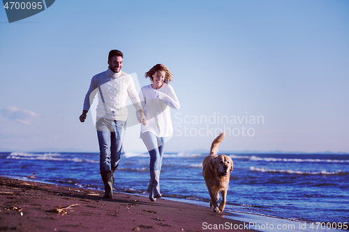 Image of couple with dog having fun on beach on autmun day