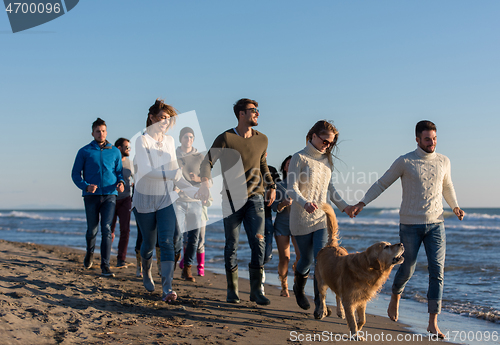 Image of Group of friends running on beach during autumn day