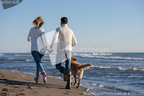 Image of couple with dog having fun on beach on autmun day