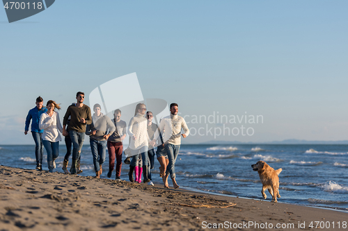 Image of Group of friends running on beach during autumn day