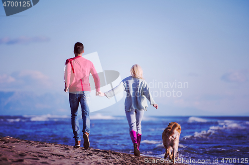 Image of couple with dog having fun on beach on autmun day