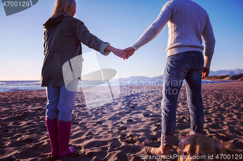 Image of couple with dog having fun on beach on autmun day