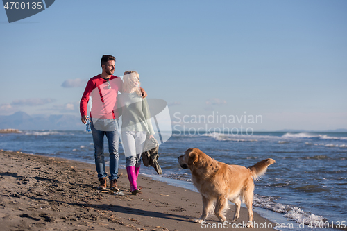 Image of couple with dog having fun on beach on autmun day