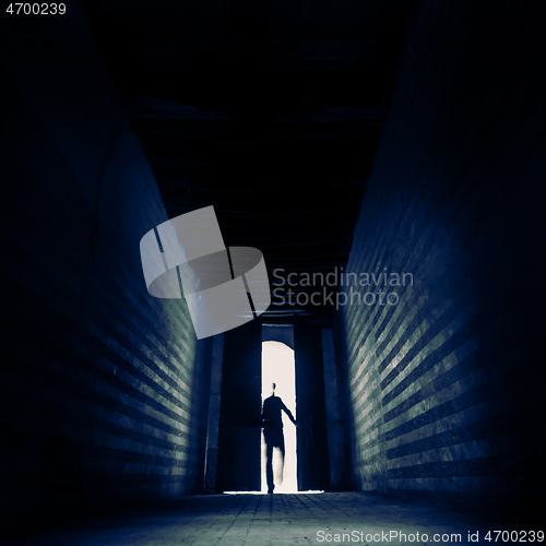 Image of Entering the unknown. Person\'s silhouette entering trough doorway to dark backlit hall. Entering the unknown.