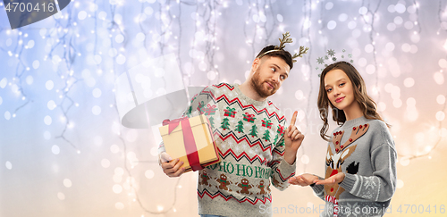 Image of happy couple in ugly sweaters with christmas gift