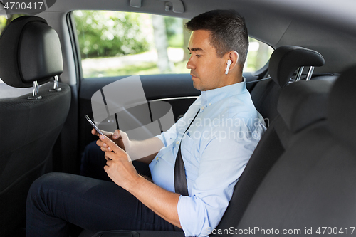 Image of passenger with earphones and cellphone in taxi car