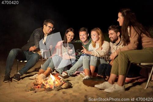 Image of friends with tablet pc at fire on beach at night