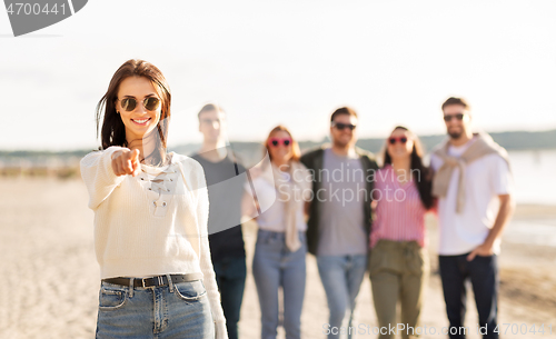 Image of happy woman with friends on beach pointing to you