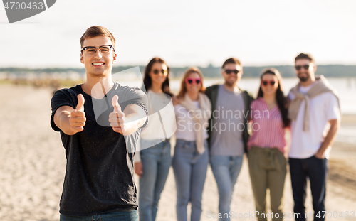 Image of happy man with friends on beach showing thumbs up