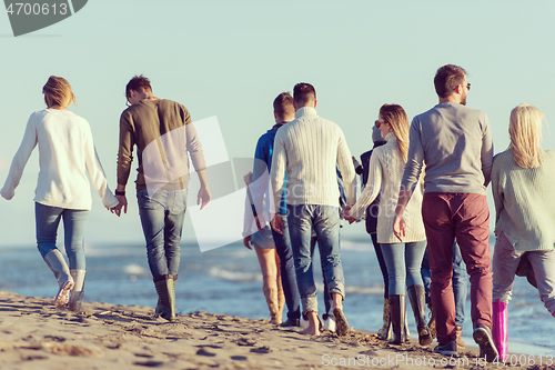 Image of Group of friends running on beach during autumn day