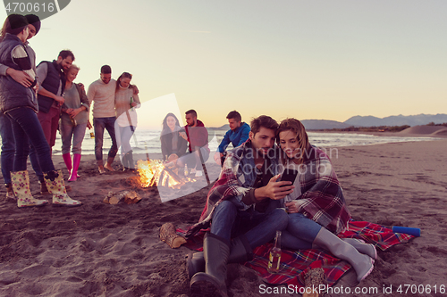 Image of Couple enjoying bonfire with friends on beach