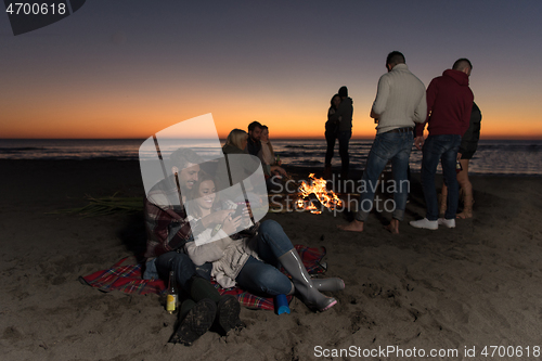 Image of Couple enjoying bonfire with friends on beach