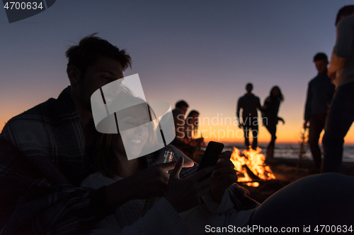 Image of Couple enjoying bonfire with friends on beach