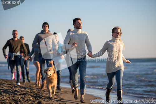 Image of Group of friends running on beach during autumn day