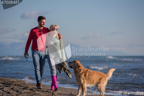 Image of couple with dog having fun on beach on autmun day