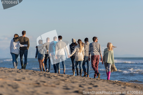 Image of Group of friends running on beach during autumn day