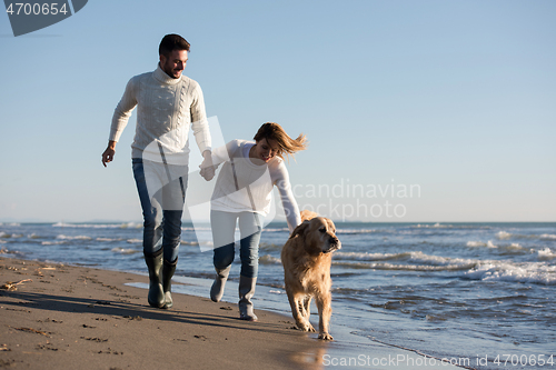 Image of couple with dog having fun on beach on autmun day