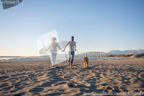 Image of couple with dog having fun on beach on autmun day