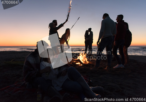 Image of Couple enjoying bonfire with friends on beach