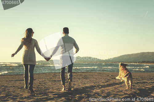 Image of couple with dog having fun on beach on autmun day