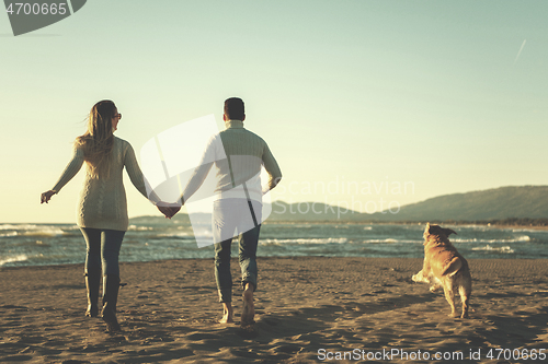 Image of couple with dog having fun on beach on autmun day