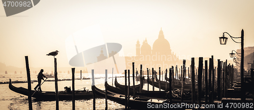 Image of Romantic Italian city of Venice, a World Heritage Site: traditional Venetian wooden boats, gondolier and Roman Catholic church Basilica di Santa Maria della Salute in the misty background