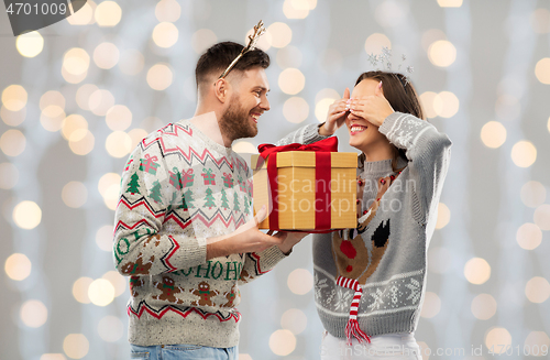 Image of happy couple in ugly sweaters with christmas gift