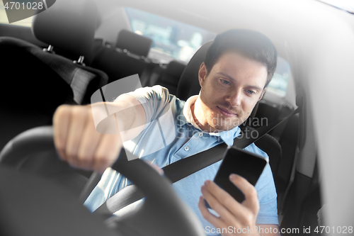 Image of man driving car and using smartphone