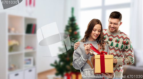 Image of happy couple in christmas sweaters with gift box