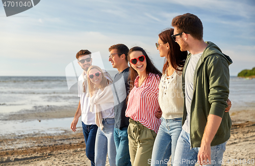 Image of happy friends walking along summer beach