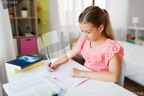 Image of student girl with book writing to notebook at home