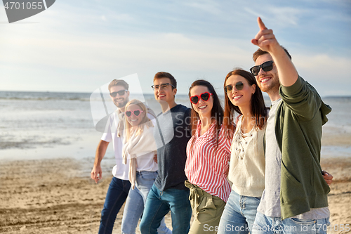 Image of happy friends walking along summer beach