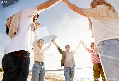 Image of happy friends holding hands on summer beach