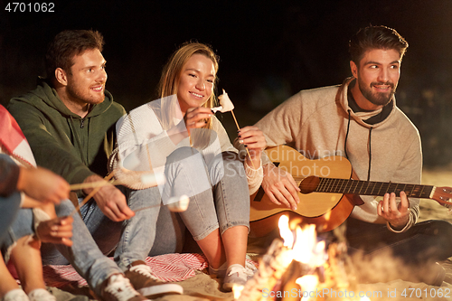 Image of friends roasting marshmallow and playing guitar