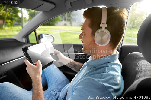 Image of passenger in headphones with tablet pc in taxi car