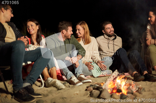 Image of group of friends sitting at camp fire on beach