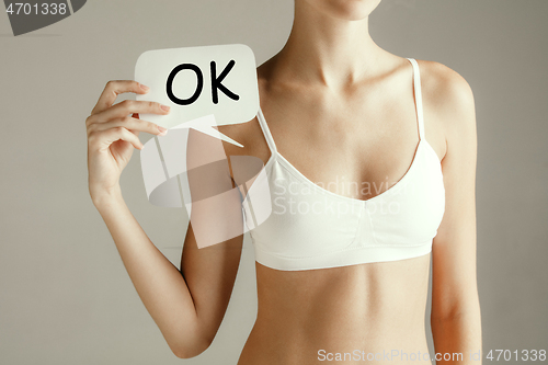 Image of Young adult woman holding paper card with sign ok.