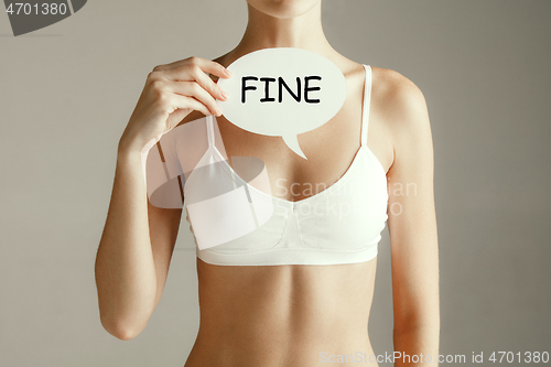 Image of Young adult woman holding paper card with word FINE.