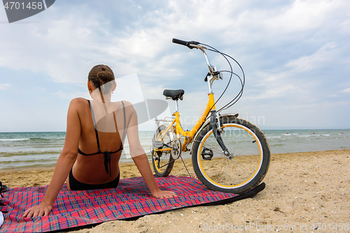 Image of A girl is resting on a sandy beach, next to there is a bicycle on which she arrived