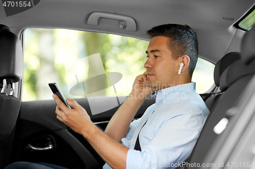 Image of passenger with earphones and cellphone in taxi car