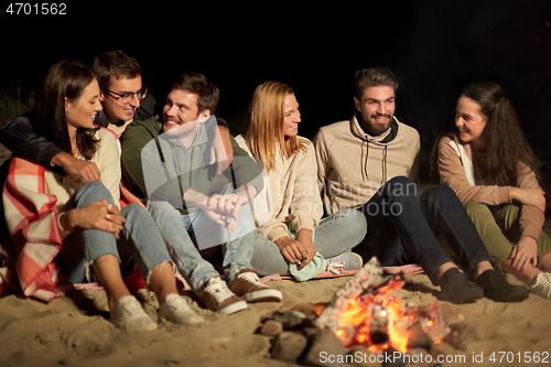 Image of group of friends sitting at camp fire on beach