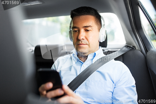 Image of passenger with headphones using smartphone in car