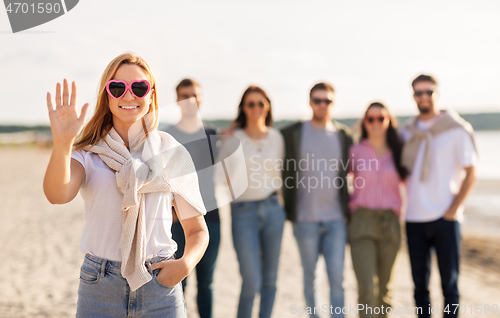 Image of woman with friends on beach in summer waving hand