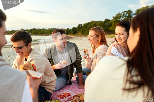 Image of happy friends eating sandwiches at picnic on beach