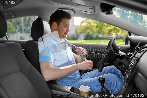 Image of man or car driver fastening seat belt