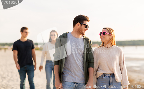 Image of happy friends walking along summer beach